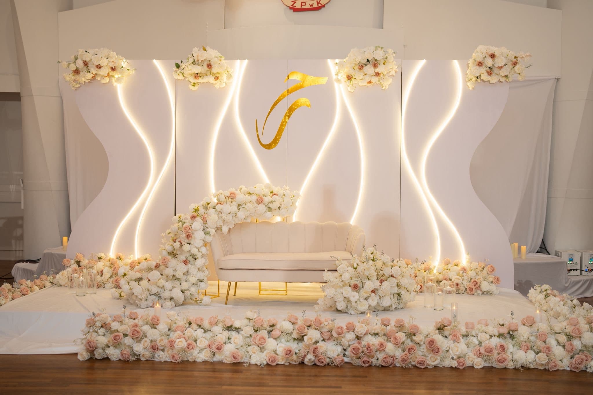 Ivory rose wedding stage with curved illuminated panels and a cream loveseat