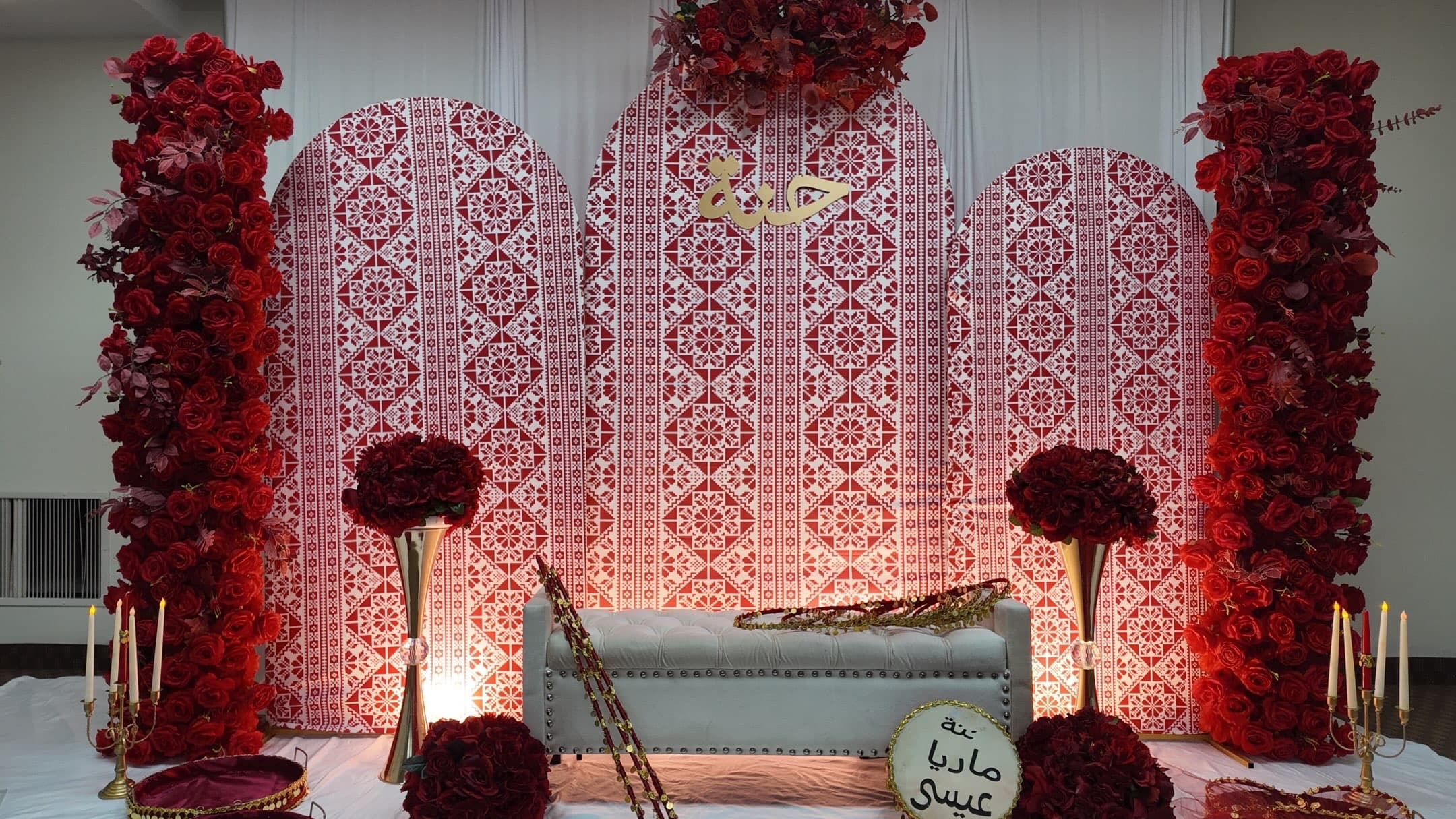 Cultural celebration stage with a patterned red backdrop, roses and a white settee